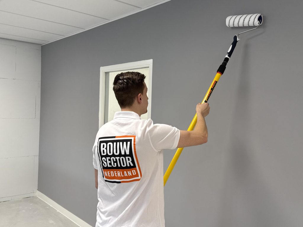 Schilder rolt een grijze wand naast een deur met een wit geschilderd kozijn