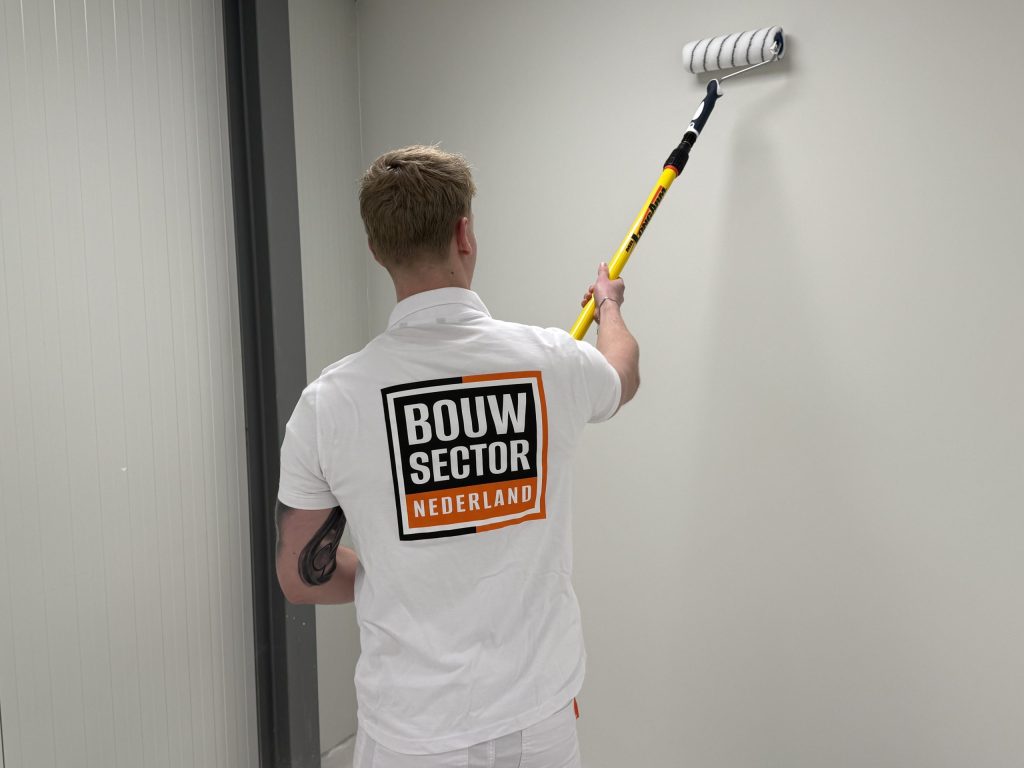 Schilder rolt een lichte wand in een smalle gang met een lange verfroller