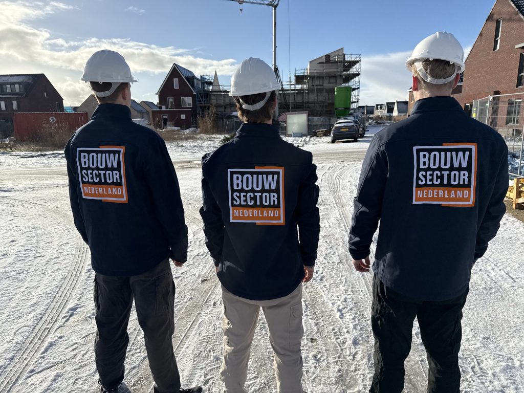 Vakmensen van Bouwsector Nederland in donkerblauwe jas en witte helm kijken uit over nieuwe bakstenen huizen